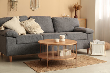 Comfortable sofa and table near beige wall in interior of light living room, closeup