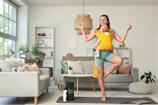 Sporty mother with her baby in sling meditating at home