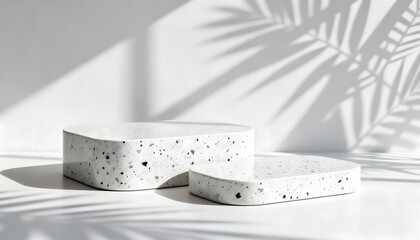Two modern terrazzo pedestals in studio lighting with palm leaf shadows