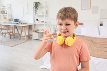 Cute little boy with headphones and glass of water in bedroom