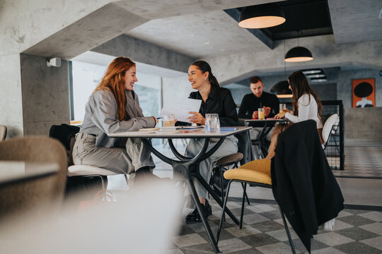 A group of coworkers and friends discuss documents around a round table in a stylish cafe. Warm, collaborative atmosphere with modern design and relaxed teamwork.