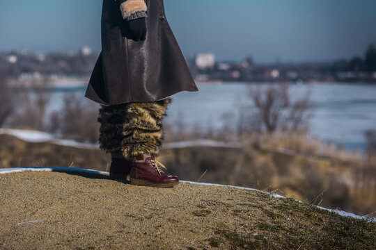 Legs of woman in fur boots on snow, closeup photo. Close-up of winter fashion: fur boots and leather coat against alpine background