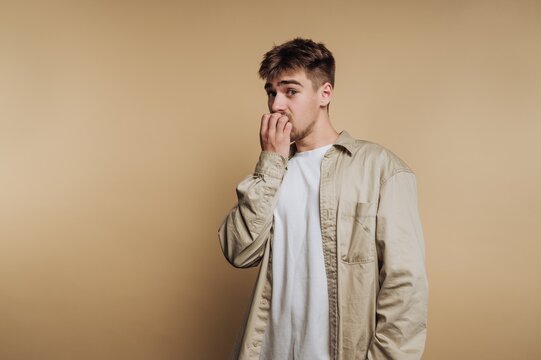 Young man showing signs of nervousness in a neutral setting while standing against a plain backdrop