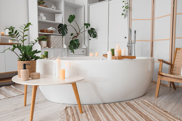 Interior of bathroom with bathtub, burning candles and plants