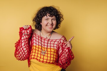 Young person poses cheerfully against a bright yellow background wearing a red mesh top and yellow dress