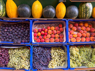 Fresh seasonal fruits including grapes, plums, peaches, and melons displayed at a local street market