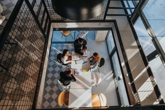 A group of colleagues gathers around a white table, reviewing documents and charts in a bright, contemporary office.