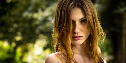 Naklejka premium Portrait of a beautiful woman with long auburn hair set against a blurred natural background