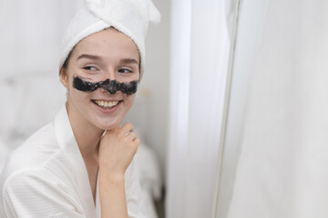 women applying blackhead removal mask on nose while looking in mirror at home. Concept of skincare routine, beauty treatment, facial care, and self care in daily life.