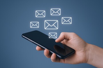 Close-up of hand holding mobile phone with email notification icons on blue background