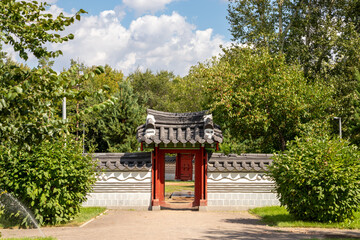 entrance to Korean garden. open red wooden doors gate under tiled roof in stone wall. Traditional Oriental Asian architecture
