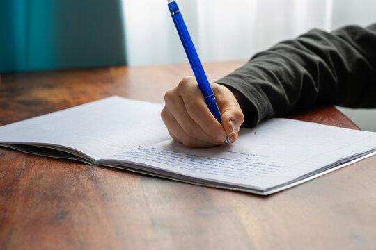 A hand writes in a notebook with a blue pen on a wooden table - Powered by Adobe