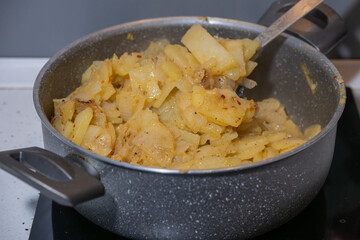 Golden slices of seasoned potatoes simmer in a pot on the stovetop, stirred gently with a metal utensil.