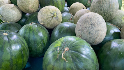 Close-up of a vibrant, fresh assortment of watermelons and sweet green cantaloupes piled high, reflecting healthy summer produce ready for market or consumption