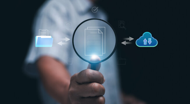 Document searching and digital data management concept. Hand holding magnifying glass show virtual document with cloud and folder symbol. Information retrieval and smart document storage systems.
