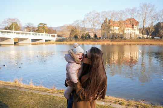 Mother Kissing Her Daughter by the Lake on Sunny Autumn Day