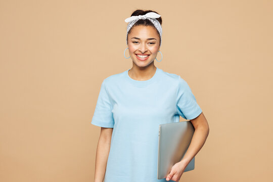 Young happy IT woman of African American ethnicity wear blue t-shirt casual clothes hold closed laptop pc computer look camera isolated on plain pastel light beige background studio Lifestyle concept