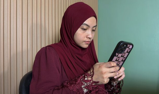 Young woman in hijab using smartphone indoors