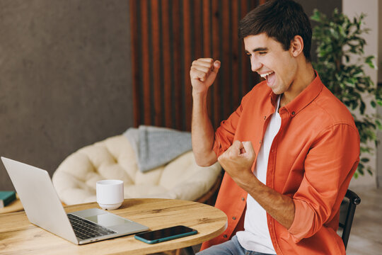 Young winner IT man wear casual clothes work or study on laptop pc computer sit alone at table in coffee shop cafe relax rest in restaurant during free time indoors. Freelance mobile office concept.