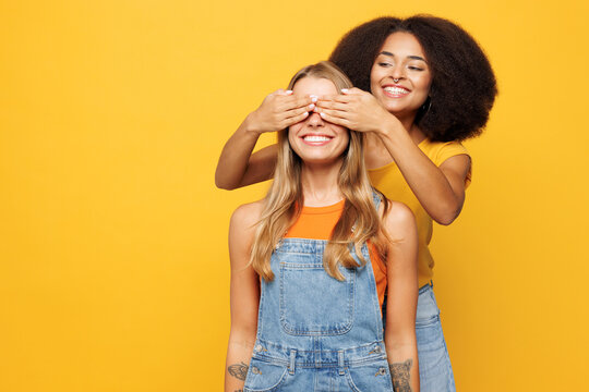 Two young friends buddies women wear denim casual clothes together close eyes with hands play guess who or hide and seek isolated on plain yellow orange background studio portrait. Lifestyle concept.