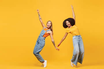 Full body two young cheerful friends buddies women wear denim casual clothes together hold hands lean back dance posing isolated on plain yellow orange background studio portrait. Lifestyle concept.