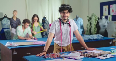 Indian young adult gen z man wear tape around neck learn new craft course look camera class room. Smart teen male boy pupil standing near desk table do casual pose staring cam enjoy day college place