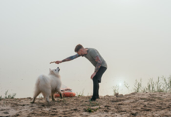 man playing with his cute samoyed dog at the lake during sunset