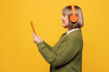 Side view elderly blonde woman wear green sweater casual clothes listen to music in headphones hold...
