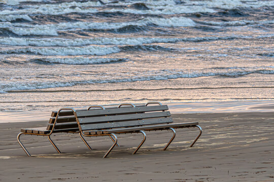 Benches by the shore at sunset with gentle waves lapping against the sand