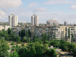 Cityscape of residential buildings with trees under a cloudy sky. This image shows a view of a city with apartment buildings and lush green trees on a sunny day