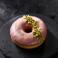Fototapeta premium Elegant Pink Glazed Donut with Pistachio Nuts on Black Slate Plate