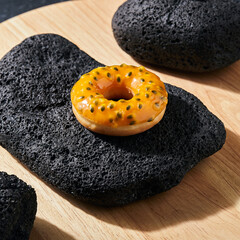 Fototapeta premium Vibrant Passion Fruit Glazed Donut on Black Lava Rock and Wooden Slab