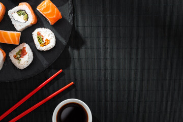 Philadelphia sushi roll salmon on slate with red chopsticks and soy sauce bowl on black bamboo mat with soft shadows.