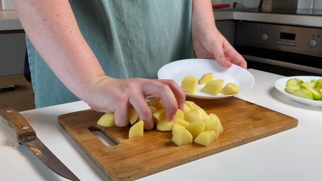 Hands gently place raw potato cubes on white plate, cooking moment filled with warm home mood, cooking process showing natural food beauty, cooking vibe ideal for lifestyle visuals.