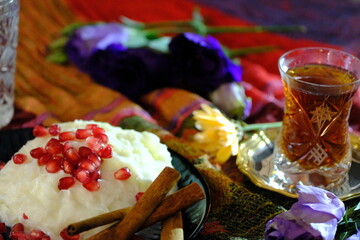 Ramadan dessert: Güllaç. Topped with pomegranate and cinnamon sticks. Tea in a crystal glass. Silver tea saucer. Purple roses and yellow daisies. Iftar table. Turkish milk desserts.
