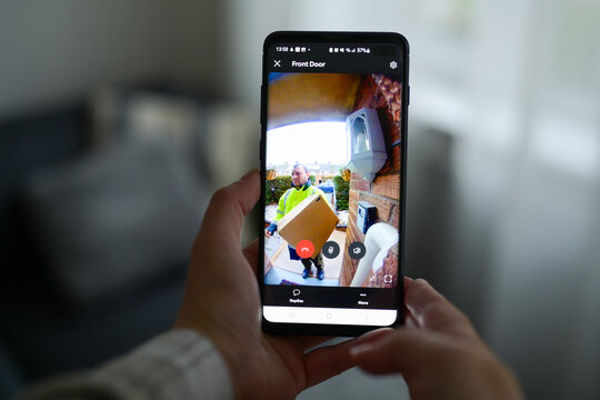 Closeup of a woman using a smartphone app to watch a delivery man dropping off a package