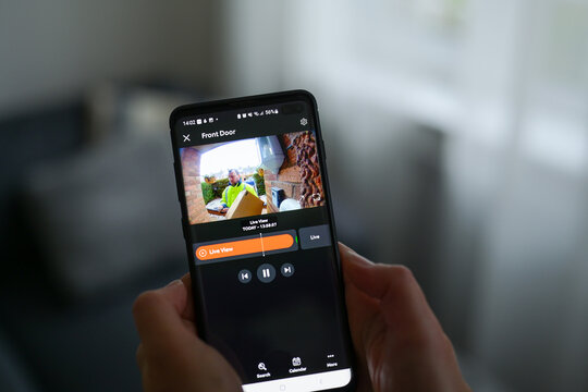 Closeup of a woman using a smartphone app to watch a delivery man dropping off a package