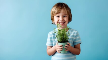 A young boy holding a potted plant against a blue background. The boy is wearing a blue and white striped shirt and has a cheerful expression on his face.