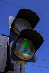 Green pedestrian signal lights up against bright blue sky in urban setting, encouraging safe...