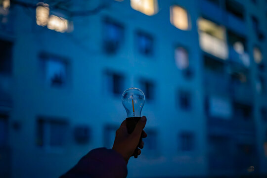 A lamp without light in a hand against the background of a multi-story building in the evening. Power outages due to the war in Ukraine.