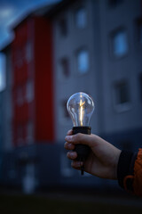 A lamp without light in a hand against the background of a multi-story building in the evening. 