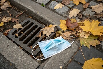 disposable mask and leaves on city drain. Urban litter trash