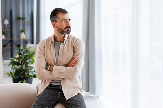 Mature man thinking looking away with arms crossed near window