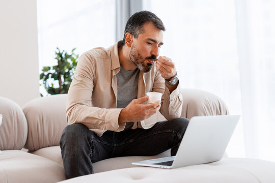 Man working from home eating yogurt lunch - Powered by Adobe