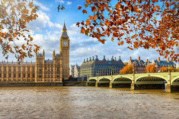 Beautiful view of the Big Ben clocktower and Westminster Palace in London during a sunny autumn day with golden leaves on the trees