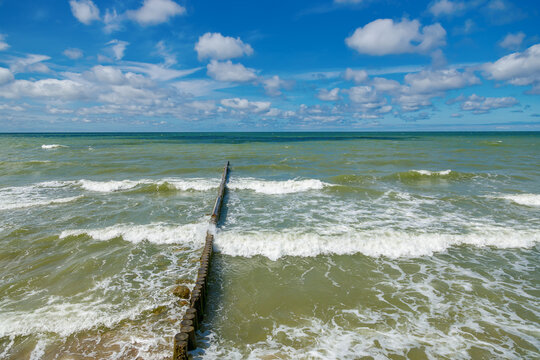 Waves of the Baltic sea breaking on a wooden groynes under a bright blue sky
