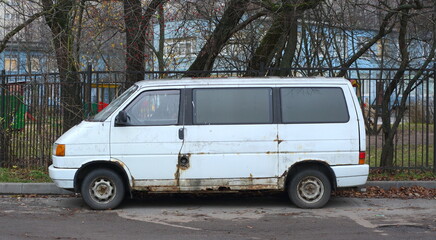 Old rusty white minivan parked near a metal lattice fence, Iskrovsky Prospekt, Saint Petersburg, Russia, November 11, 2025