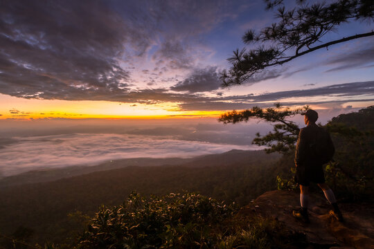 A young adventurer stands on a high cliff of a mountain peak, looking at the beautiful morning landscape at Pha Nok Aen, Phu Kradueng National Park. Travel and Lifestyle Concept	