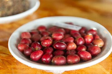 Close-up of fresh, ripe coffee cherries in a white bowl, showcasing their vibrant red color and plump texture before processing