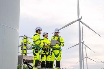 Engineer team in safety harnesses, collaborating on maintenance platform for wind turbine inspection. On-site service team with PPE, planning and inspecting wind turbines from a maintenance lift.